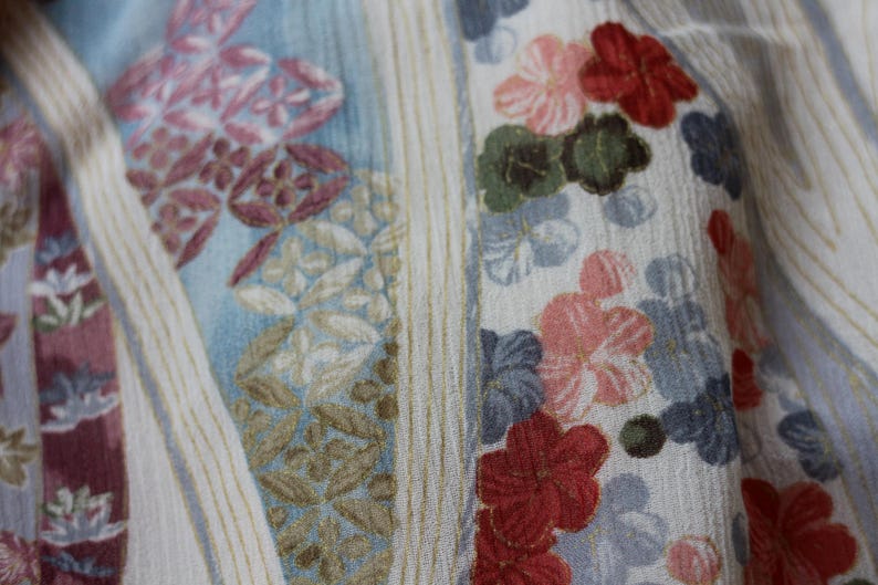 May include: Close-up of a fabric with a floral pattern. The design features flowers in shades of red, pink, and blue, set against a light background with vertical stripes. The fabric has a textured appearance, suggesting a soft material.