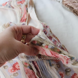 May include: A floral patterned garment with a zipper closure. The fabric features a mix of colors including red, pink, and blue. The garment is held by a hand with a gold ring.