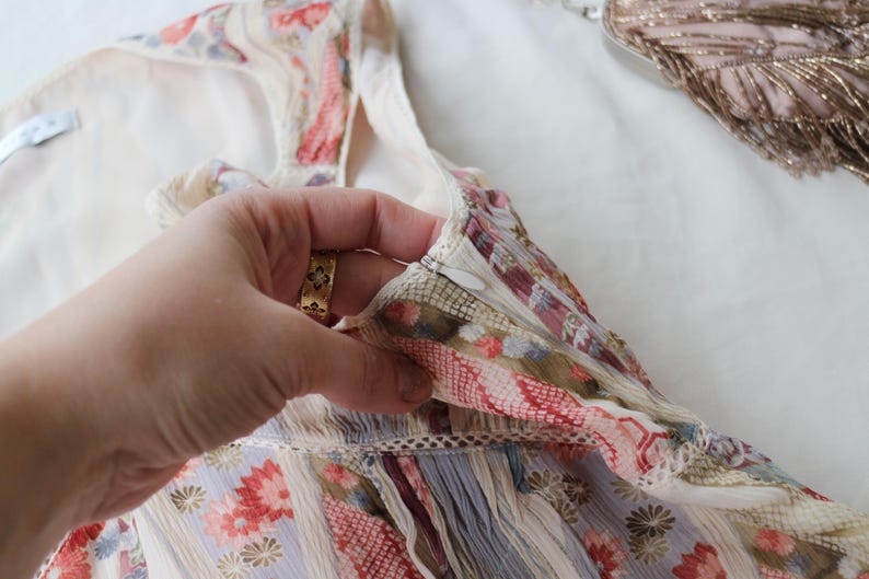 May include: A floral patterned garment with a zipper closure. The fabric features a mix of colors including red, pink, and blue. The garment is held by a hand with a gold ring.
