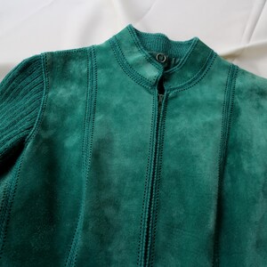 May include: A teal suede jacket with a ribbed knit sleeve and collar. The jacket has a full zipper and vertical stitched seams. The jacket is a solid teal color.
