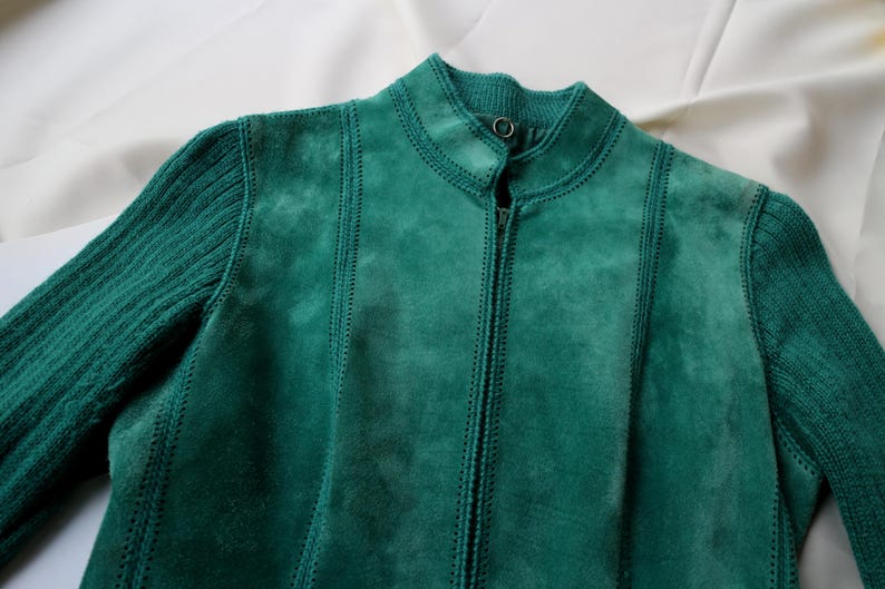 May include: A teal suede jacket with a ribbed knit sleeve and collar. The jacket has a full zipper and vertical stitched seams. The jacket is a solid teal color.