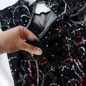 May include: Black dress with silver and red sequin and bead embellishments. The dress features a keyhole back and a zipper closure. The design includes floral and leaf patterns.