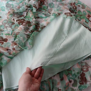 May include: A floral print dress with a light green lining. The outer layer features a pattern of green, brown, and peach-colored flowers on a sheer fabric. The dress is partially visible, with the lining and outer layer separated.