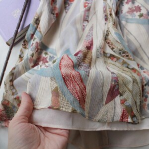 May include: A flowing, patterned fabric with a mix of floral and geometric designs in shades of cream, red, blue, and green. The fabric appears to be layered, with a soft, light texture. The overall aesthetic suggests a vintage or bohemian style.