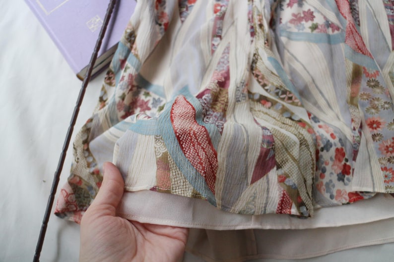 May include: A flowing, patterned fabric with a mix of floral and geometric designs in shades of cream, red, blue, and green. The fabric appears to be layered, with a soft, light texture. The overall aesthetic suggests a vintage or bohemian style.