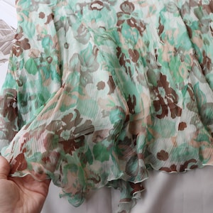 May include: A sheer, flowing garment with a floral pattern in shades of green, brown, and peach. The fabric appears lightweight and delicate, with a ruffled edge. The garment is likely a skirt or a dress.