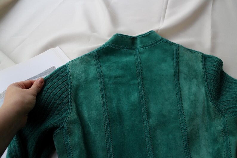 May include: A teal green suede jacket with ribbed knit sleeves and collar. The back of the jacket features vertical stitched panels. The jacket is displayed on a white surface.