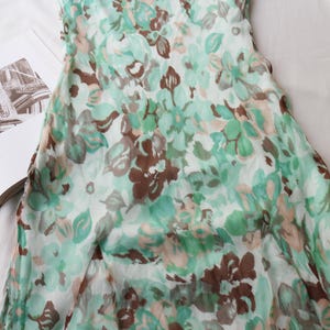 May include: A floral print dress in shades of green, brown, and white. The dress features a delicate pattern of flowers and leaves. The fabric appears lightweight and flowing, suggesting a summer garment. The dress is partially visible, with the top portion in focus.