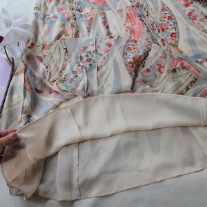 May include: A light-colored dress with a floral and geometric pattern. The dress features a layered design with a sheer outer layer and a solid-colored lining. The fabric has a soft, flowing appearance, and the dress appears to be in good condition.