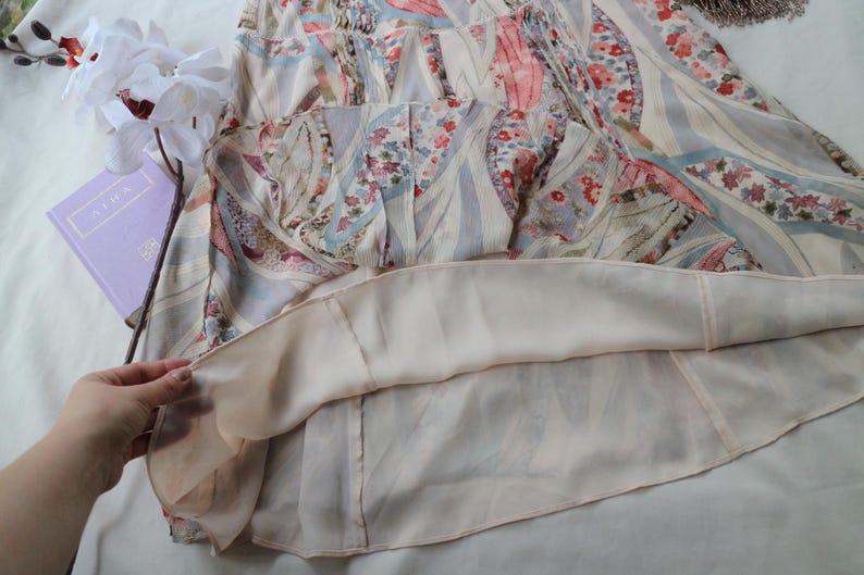 May include: A light-colored dress with a floral and geometric pattern. The dress features a layered design with a sheer outer layer and a solid-colored lining. The fabric has a soft, flowing appearance, and the dress appears to be in good condition.