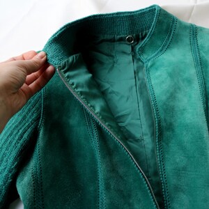 May include: Teal suede jacket with a ribbed knit collar and sleeves. The jacket has a zipper closure and vertical stitched panels. The lining is a matching teal color. The jacket is displayed on a white surface.