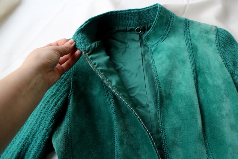 May include: Teal suede jacket with a ribbed knit collar and sleeves. The jacket has a zipper closure and vertical stitched panels. The lining is a matching teal color. The jacket is displayed on a white surface.