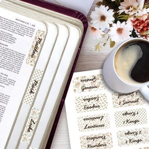 Könnte beinhalten: Ein Set aus selbstklebenden Bibel-Registerkarten mit Blumenmuster in Beige- und Grüntönen. Die Karten sind mit schwarzem Text bedruckt, darunter Matthew, Mark, Luke, Genesis, Exodus, Leviticus, Numbers, 2 Samuel, 1 Kings und 2 Kings, dargestellt auf einer Bibelseite und einem Bogen.