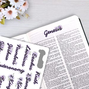 May include: A sheet of adhesive Bible index tabs featuring black cursive text on a white background with purple floral accents. The tabs include names like Genesis, Exodus, Leviticus, Numbers, Deuteronomy, Joshua, Ruth, and Kings.