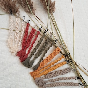 Peut inclure: Un ensemble de porte-clés en macramé faits main dans différentes couleurs, notamment beige, rouge, vert, orange et marron. Chaque porte-clés présente un design tressé et un pompon à l'extrémité.