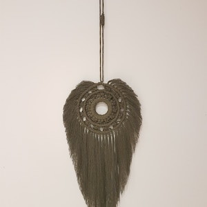 Peut inclure: Une suspension murale en macramé verte avec un motif circulaire et des franges.