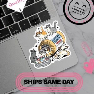 May include: A sticker featuring a cartoon illustration of cats spilling out of a pill bottle labeled "Serotonin Booster." The sticker has a playful design with the text "Cute Aggression" and "Quality."