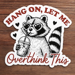 May include: A black and white sticker featuring a raccoon wearing heart-shaped sunglasses and drinking from a beverage cup. The sticker has the text "HANG ON, LET ME Overthink This" in a red, stylized font, with black heart accents.
