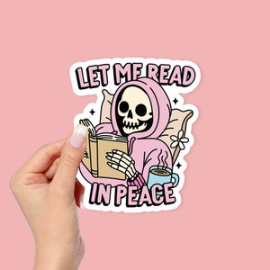 May include: A pink sticker with a skeleton wearing a pink hoodie and reading a book. The text on the sticker says "Let me read in peace".