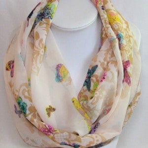 Könnte beinhalten: Ein weißer Chiffon-Schal mit einem gold-weißen Damastmuster und bunten Schmetterlingsdesigns.