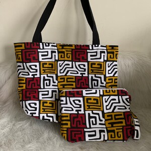 May include: A black tote bag with a white, red, and gold geometric pattern. The bag comes with a matching smaller pouch.