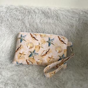 May include: A white zippered pouch with a seashell and starfish print. The pouch has a brown strap.
