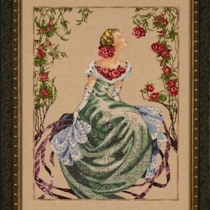 Może przedstawiać: Wzór do haftu krzyżykowego przedstawiający kobietę w zielonej sukni z kwiatowym wzorem, otoczoną winoroślą z różowymi różami.