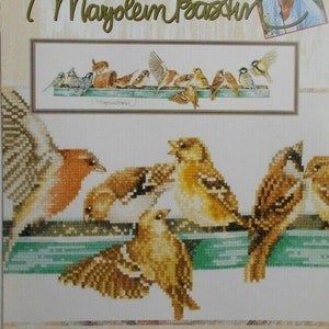 May include: Cross stitch pattern featuring a group of birds perched on a branch. The pattern is titled "The Pecking Order" and is by designer Marjolein Bastin. The pattern is from the Lanarte by Leisure Arts brand.