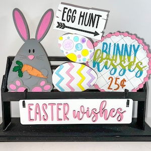 May include: A black wooden stand with a gray bunny holding a carrot, a sign that says "Egg Hunt", a sign that says "Bunny Kisses 25¢", and a sign that says "Easter Wishes".