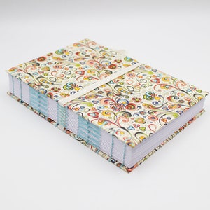 Könnte beinhalten: Ein farbenfrohes, floral gemustertes Tagebuch mit einem weißen Bandverschluss. Das Tagebuch ist mit blauen Nähten gebunden und hat weiße Seiten.