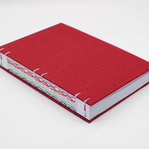 May include: A red fabric-covered journal with a rainbow of coloured thread stitching along the spine.