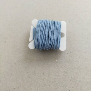 May include: A spool of light blue thread wound around a white plastic bobbin.