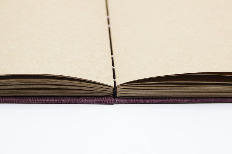 May include: A closed book with a purple fabric cover and brown pages. The book is open to reveal the pages.