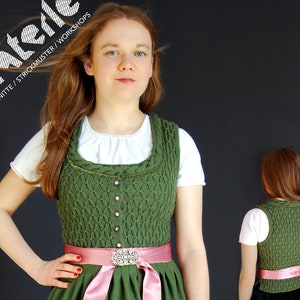 Könnte beinhalten: Eine grüne Strickweste mit einem rosa Band und einer silbernen Schnalle. Die Weste hat ein Zopfmuster und wird über einem weißen Hemd getragen.