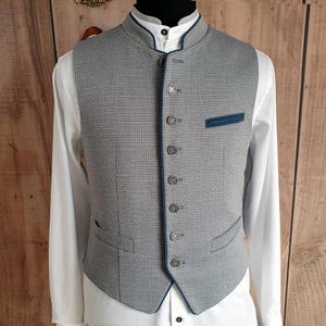 Puede incluir: Un chaleco gris estampado con cuello mao y ribete azul oscuro. El chaleco tiene botones decorativos y un peque&ntilde;o bolsillo con ribete azul oscuro. Se lleva sobre una camisa blanca.