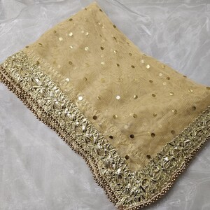 May include: A gold net dupatta with a gold embroidered border and sequins. The dupatta is folded and laid on a white surface.