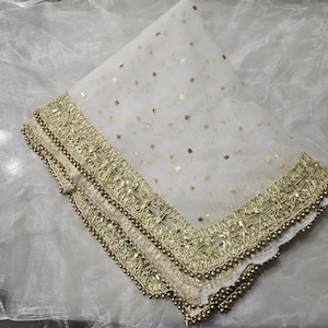 May include: A white sheer scarf with gold embroidered trim and small gold dots. The trim features a beaded edge.