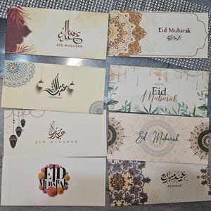 May include: Eight different Eid Mubarak greeting cards with various designs. Some cards feature intricate mandala patterns, while others have calligraphy and floral motifs. The cards are all in shades of beige, brown, and gold.