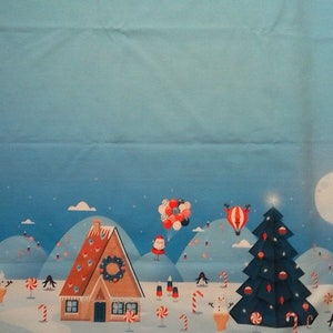 Op de afbeelding: Een blauwe en witte kerststof met een peperkoekhuis, een kerstboom, een luchtballon en een sneeuwpop. De stof is versierd met snoepstokken, sterren en sneeuwvlokken.
