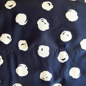 Op de afbeelding: Close-up van een marineblauwe stof met een herhalend patroon van gebroken witte, wolkvormige vormen. De vormen zijn onregelmatig van vorm en verspreid over het oppervlak, waardoor een textuur ontstaat. De stof lijkt katoen of een vergelijkbaar materiaal te zijn.