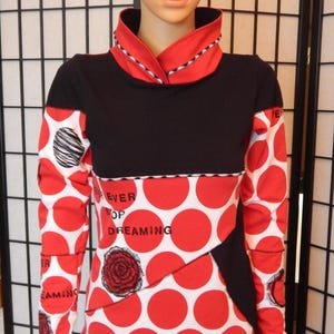 Könnte beinhalten: Langärmliges Oberteil mit schwarzem Oberteil und rot-weißem Polka-Dot-Muster. Die Ärmel und der untere Körper haben große rote Polka-Dots auf weißem Grund. Das Oberteil enthält den Text "EVER STOP DREAMING" und eine Rosengrafik.