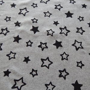 Puede incluir: Primer plano de tela gris con un patrón repetitivo de estrellas negras. Algunas estrellas son sólidas, otras están delineadas. Las estrellas varían en tamaño y están dispersas sobre el material.