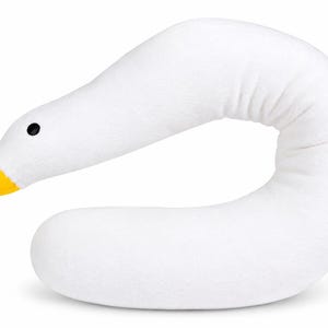 May include: A white plush pillow shaped like a goose neck with a curved body. The head features a bright yellow beak and a small, round black eye. The soft, textured fabric forms a continuous, elongated shape that mimics the neck and head of a bird.
