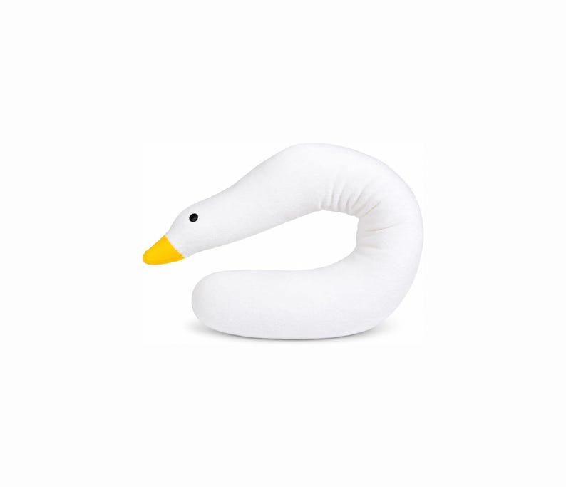 May include: A white plush pillow shaped like a curved goose neck and body. The pillow features a bright yellow beak and a small, round black eye. The soft, stuffed fabric forms a continuous, elongated loop that mimics the graceful posture of a goose.