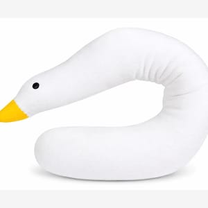 May include: A white plush pillow shaped like a long, curved goose neck. The pillow features a bright yellow beak and a small, round black eye. The soft, elongated body curves into a U-shape, mimicking the graceful posture of a goose's neck and head.
