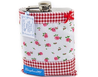Peut inclure: Une flasque en métal recouverte d'un tissu blanc à motif de roses roses, avec une bordure à carreaux rouges et blancs en haut et en bas. Un petit nœud en ruban rouge est fixé en haut à droite. Une étiquette bleue porte le nom Ringelsuse.