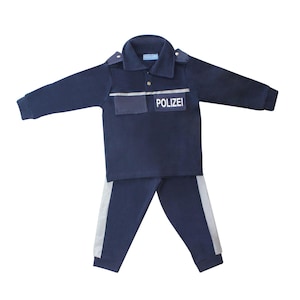 Può includere: Un costume da poliziotto blu navy per bambini. L'abito comprende una camicia a maniche lunghe con una striscia bianca e la scritta "POLIZEI" sul petto, e pantaloni abbinati con strisce bianche sui lati.
