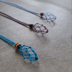 May include: Three necklaces with crystal point holders. The necklaces are made of braided cord and have wooden beads. The crystal point holders are made of knotted cord and come in blue, purple, and teal.