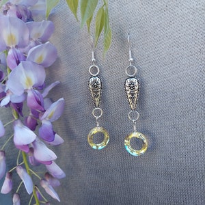 May include: A pair of silver dangle earrings with a teardrop-shaped charm and a round, yellow crystal bead. The earrings have a delicate, feminine design.
