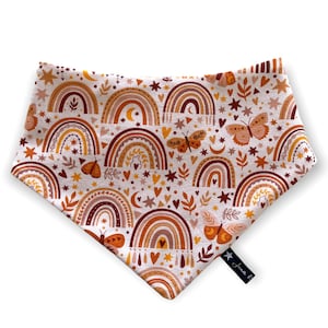 May include: A white bandana with a colorful pattern of rainbows, butterflies, stars, and hearts. The bandana is trimmed with a brown border.